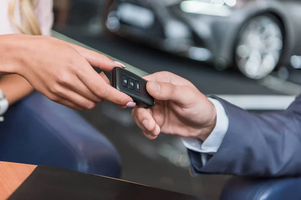 Partial view of dealership salon seller giving car key to woman in auto salon — Stock Photo