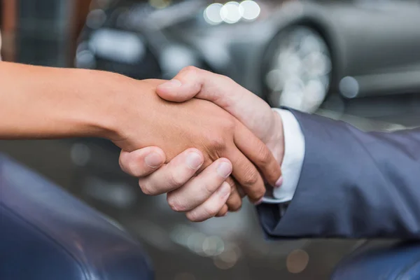 Cropped shot of dealership salon shop assistant and female customer shaking hands in auto salon — Stock Photo