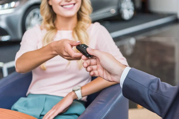 Partial view of dealership salon seller giving car key to smiling woman in auto salon — Stock Photo