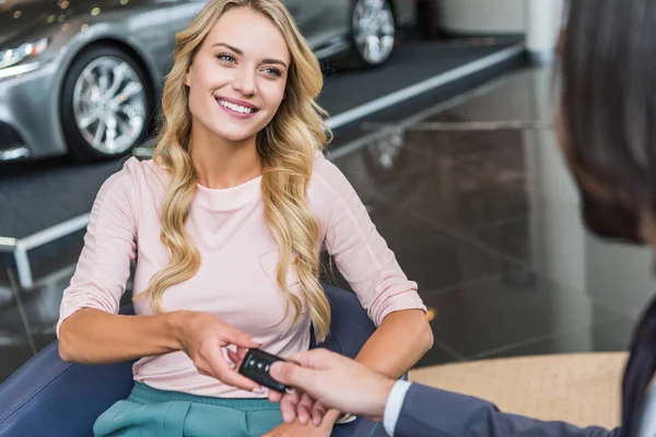 Vue partielle du vendeur de salon de concession donnant la clé de voiture à la femme souriante dans le salon de l'automobile — Photo de stock