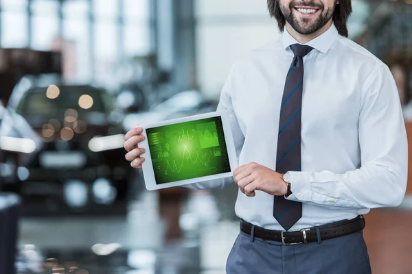 Tiro recortado de vendedor de salão de concessionária sorrindo em desgaste formal mostrando tablet com diagrama gráfico nas mãos — Fotografia de Stock