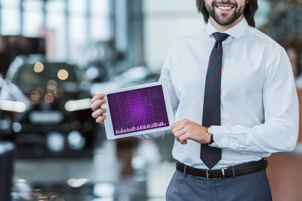 Cropped shot of smiling dealership salon seller in formal wear showing tablet with graphic diagram in hands — Stock Photo