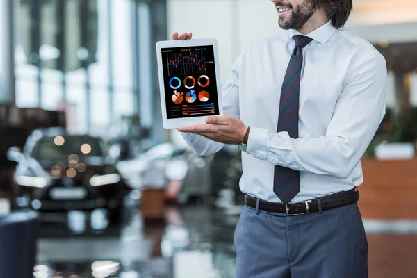 Teilansicht des Autohauses Salon Verkäufer in formaler Kleidung zeigt Tablet mit Infografik in den Händen — Stockfoto