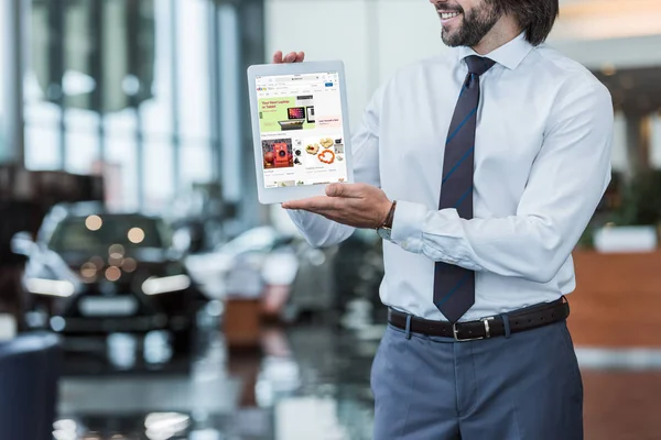 Partial view of dealership salon seller in formal wear showing tablet with ebay website in hands — Stock Photo