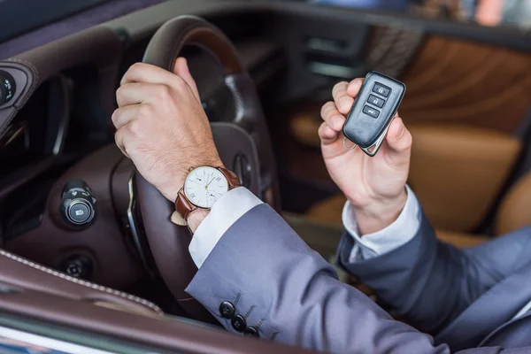 Plan recadré de l'homme d'affaires avec clé de voiture à la main assis dans une voiture neuve dans le salon de concession — Photo de stock