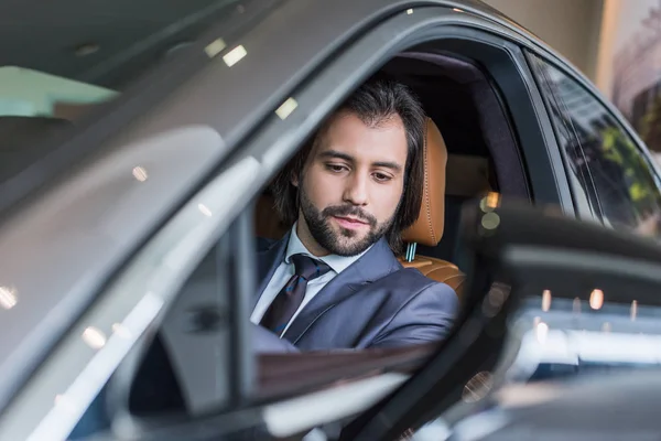 Uomo d'affari seduto in una nuova auto per test drive nel salone di concessionaria — Foto stock