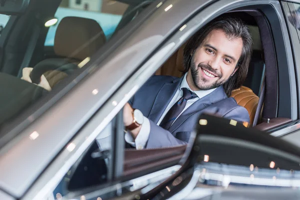 Porträt eines Geschäftsmannes, der im neuen Auto zur Probefahrt im Autohaus-Salon sitzt — Stockfoto