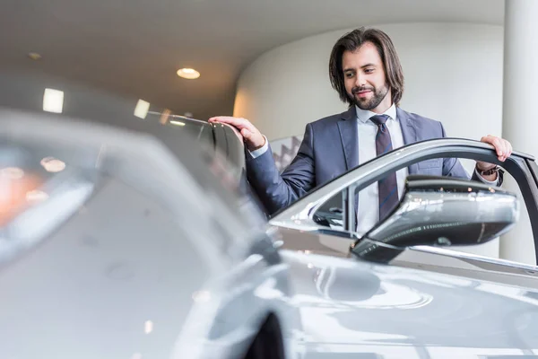 Retrato de hombre de negocios con estilo de pie en el nuevo coche en el salón de concesionarios - foto de stock