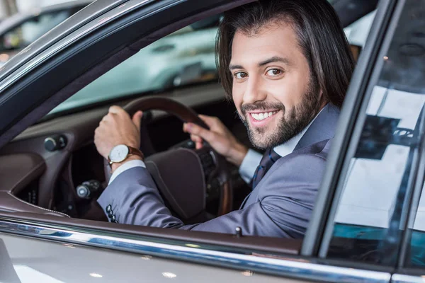 Homme d'affaires souriant assis dans une voiture neuve pour un essai routier dans le salon de concession — Photo de stock