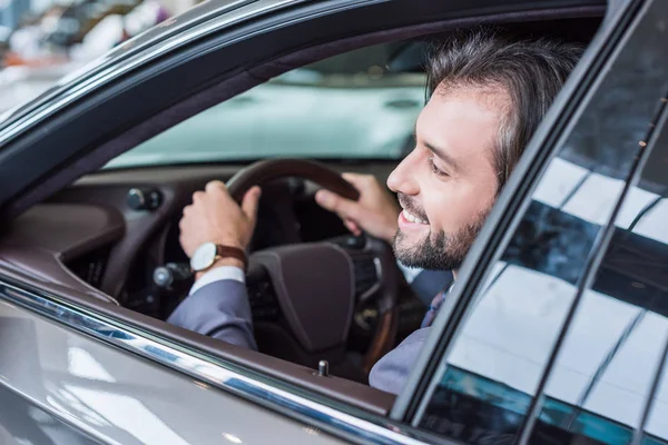 Sonriente hombre de negocios sentado en coche nuevo para la prueba de conducción en el salón de concesionarios - foto de stock