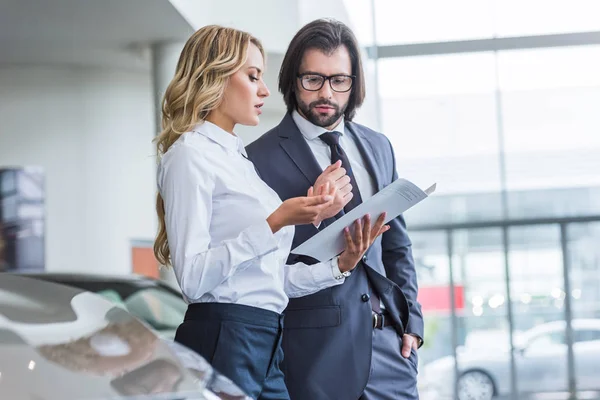 Vista lateral del vendedor y hombre de negocios con estilo en el salón de concesionarios - foto de stock