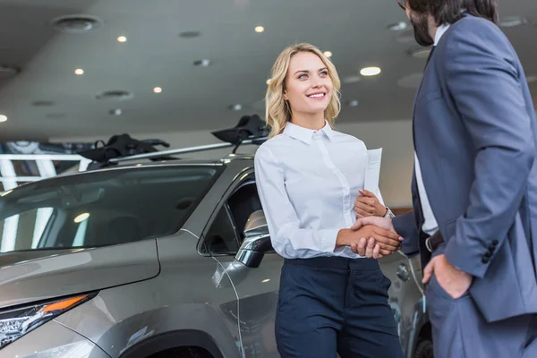 Partial view of smiling auto salon seller and businessman shaking hands at dealership salon — Stock Photo