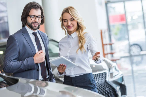 Vendeur de salon automobile femelle avec tablette aidant l'homme d'affaires à choisir la voiture au salon de concession — Photo de stock