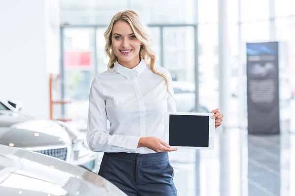 Portrait de vendeur souriant montrant tablette avec écran blanc dans les mains dans le salon de concession — Photo de stock