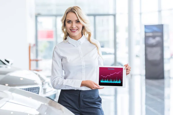 Portrait of smiling seller showing tablet with trading sign in hands in dealership salon — Stock Photo