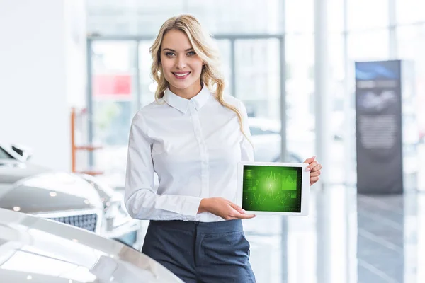 Retrato de vendedor sorrindo mostrando tablet com diagrama gráfico em mãos no salão de concessionárias — Fotografia de Stock