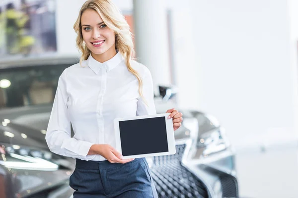 Ritratto di venditore sorridente che mostra tablet con schermo bianco in mano nel salone di concessionaria — Foto stock