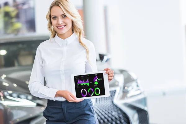 Portrait of smiling seller showing tablet with infographic in hands in dealership salon — Stock Photo