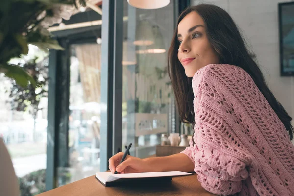 Sorridente giovane donna prendere appunti nel libro di testo a tavola nel caffè — Foto stock