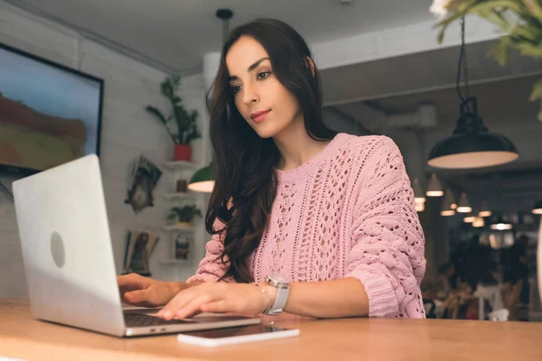 Beautiful female freelancer working on laptop while sitting at table with smartphone and coffee cup in cafe — Stock Photo