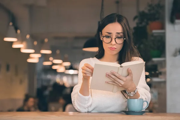 Triste beau livre de lecture femme à table avec tasse de café dans le café — Photo de stock