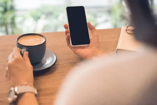 Частичный вид женщины с чашкой кофе с помощью смартфона за столом в кафе — стоковое фото