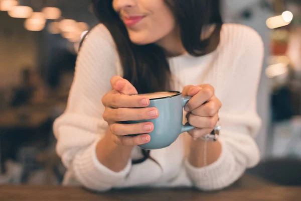 Vista parcial de la mujer sosteniendo la taza de café en la mesa en la cafetería - foto de stock