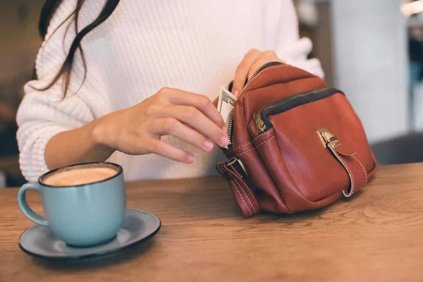 Vue partielle de la femme tirant de l'argent du sac à table avec tasse de café dans le café — Photo de stock