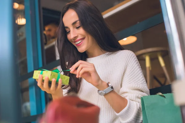 Sonriente joven mujer desatando caja de regalo en la cafetería - foto de stock