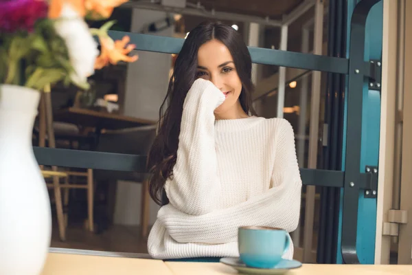 Sorrindo mulher bonita sentada à mesa com xícara de café no café — Fotografia de Stock