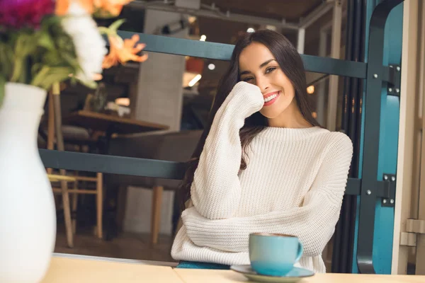 Glücklich attraktive junge Frau blickt in die Kamera am Tisch mit Kaffeetasse im Café — Stockfoto