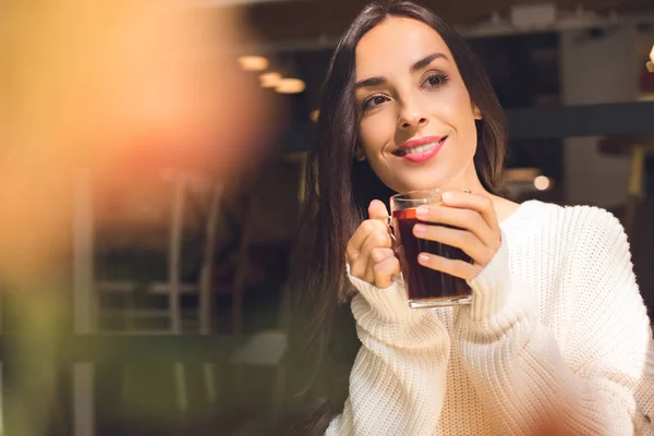 Foco seletivo da mulher feliz segurando xícara de vinho quente à mesa no café — Fotografia de Stock