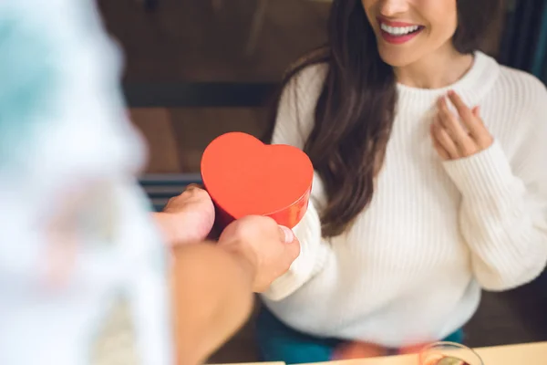 Immagine ritagliata di uomo che presenta scatola regalo a forma di cuore alla ragazza felice a tavola nel caffè — Foto stock