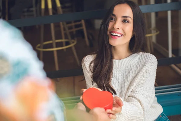 Partial view of man presenting heart shaped gift box to happy girlfriend at table in cafe — Stock Photo