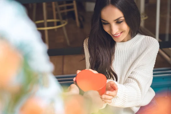 Image recadrée de l'homme présentant boîte cadeau en forme de coeur à la jeune copine attrayante à la table dans le café — Photo de stock