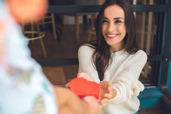 Partial view of man presenting heart shaped gift box to happy girlfriend at table in cafe — Stock Photo