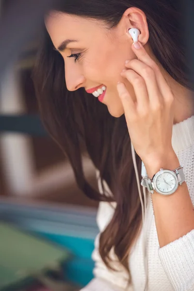 Selective focus of smiling young woman putting on earphones in cafe — Stock Photo