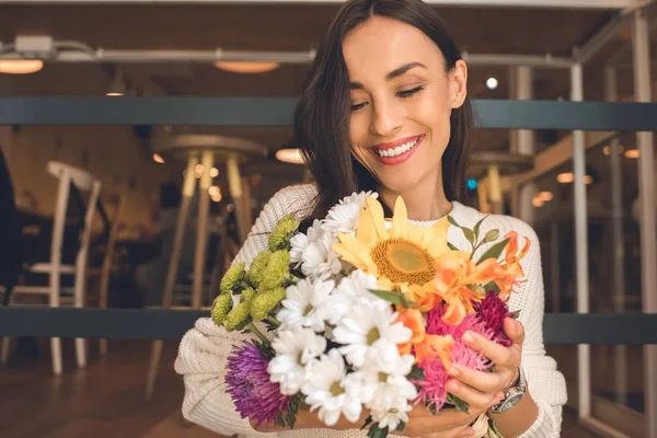 Selektiver Fokus einer glücklichen jungen Frau mit einem bunten Strauß aus verschiedenen Blumen im Café — Stockfoto