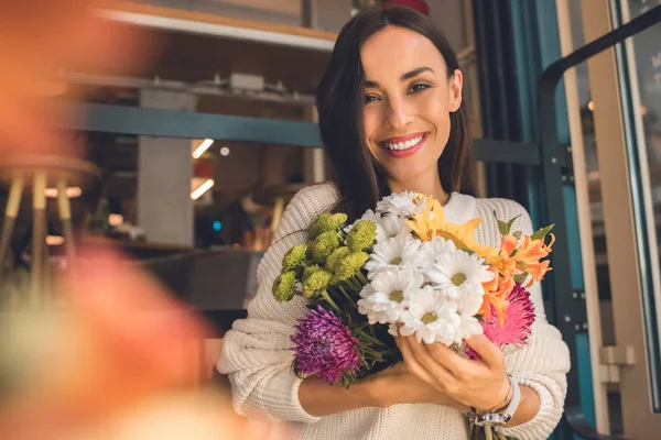 Portrait of smiling young woman holding colorful bouquet from various flowers in cafe — Stock Photo