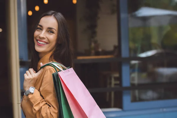 Retrato de mujer hermosa con estilo con bolsas de compras sobre el hombro mirando hacia la calle de la ciudad - foto de stock