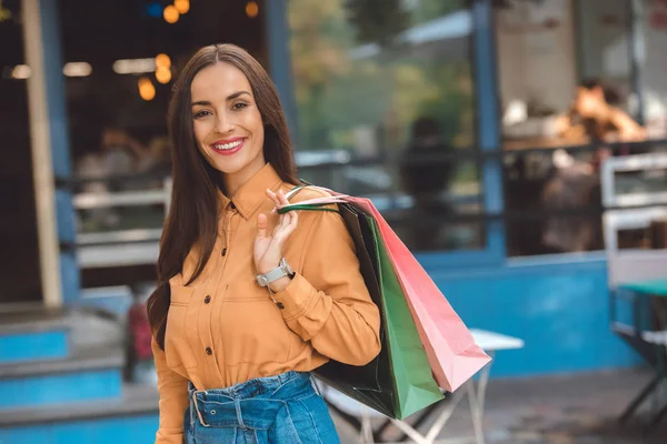 Retrato de sonriente elegante comprador femenino con bolsas de compras en la calle de la ciudad - foto de stock