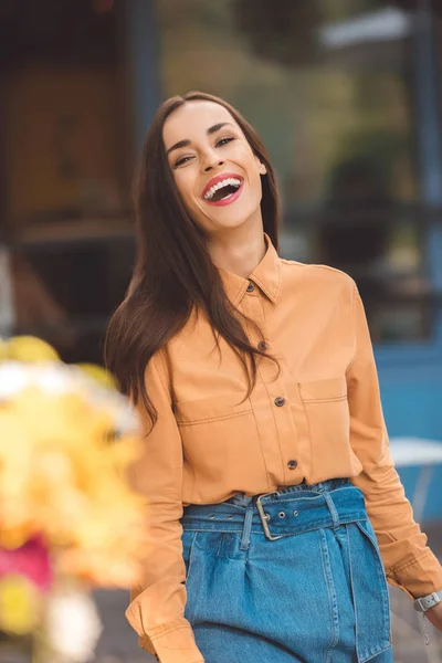 Selective focus of laughing fashionable woman looking at camera at city street — Stock Photo