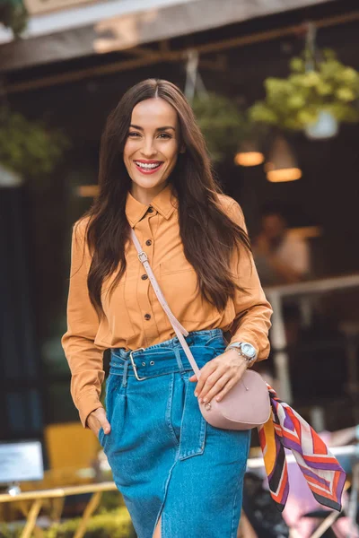 Модная молодая женщина со стильной сумочкой смотрит в камеру на городской улице — стоковое фото