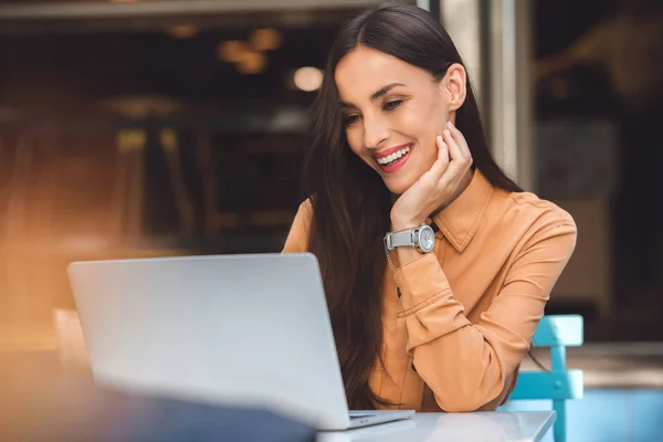 Giovane freelance sorridente che lavora a computer portatile a tavola in caffè a strada urbana — Foto stock