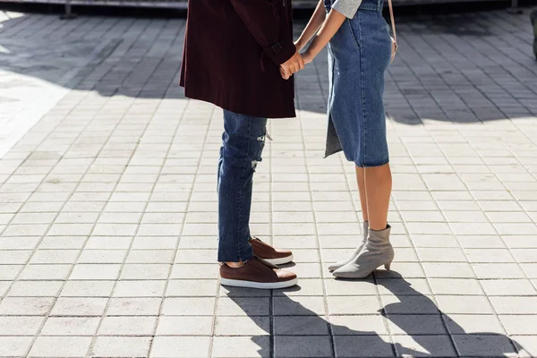 Imagen recortada de pareja en traje de otoño tomados de la mano en la calle en la ciudad - foto de stock