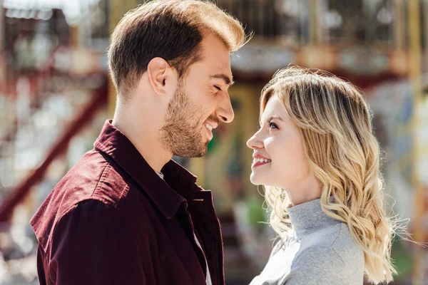 Portrait of affectionate couple in autumn outfit looking at each other near carousel in amusement park — Stock Photo