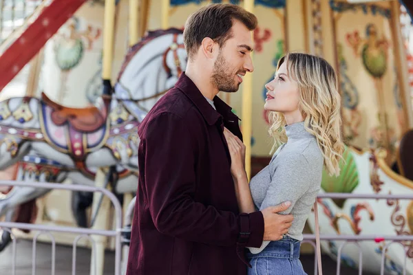 Side view of romantic couple in autumn outfit cuddling near carousel in amusement park — Stock Photo