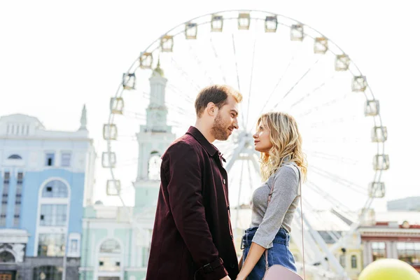 Side view of couple in autumn outfit holding hands with observation wheel on background — Stock Photo
