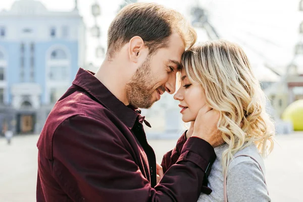 Side view of couple in autumn outfit touching with foreheads in city — Stock Photo
