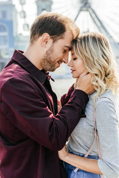 Side view of affectionate couple in autumn outfit touching with foreheads in city — Stock Photo